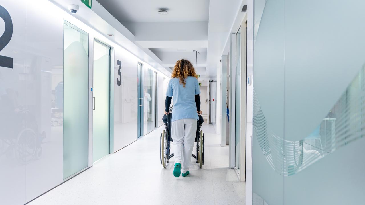 Vista posterior de la infermera empenyent una cadira de rodes per l'hospital